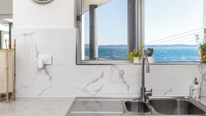 A kitchen with a large window, a sink, and a clock on the wall. - Bayview Towers 10 With Harbour Views (Nelson Bay)