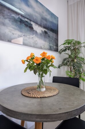 A round table with a woven placemat, a vase with orange roses, and a large abstract painting on the wall.