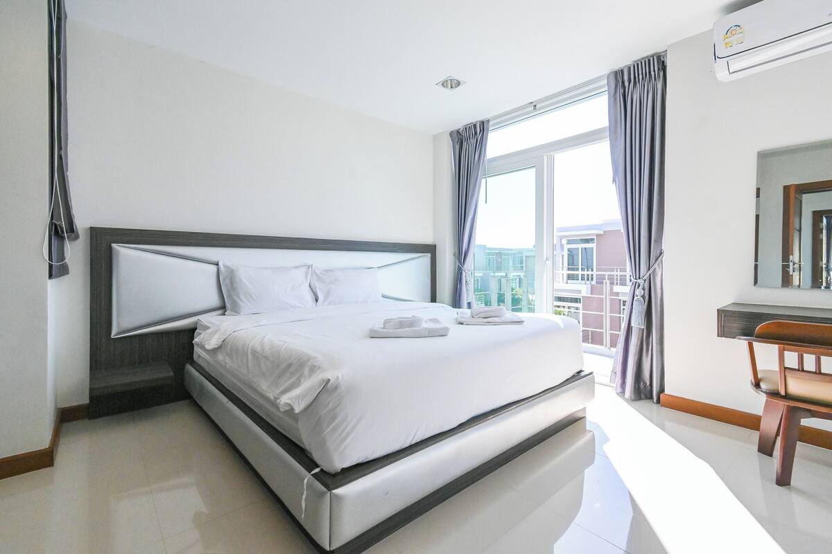 A modern hotel room with a large bed, a desk, and a view of the city.