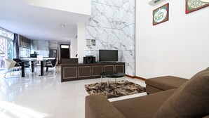 Ein modernes Wohnzimmer mit einer Couch, einem Couchtisch und einem Fernseher. Es gibt eine Küchenzeile mit Schränken und einem Esstisch.