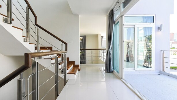 Ein modernes Hotelinnere mit Treppe, einem Balkon mit Glastür und Blick ins Freie.