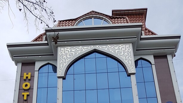 Et hotel med en stor glasfacade, et tydeligt skilt med teksten "KHUJAND STAR HOTEL" og en mannequin i kjole foran indgangen.