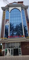Un hotel con un amplio ventanal de vidrio, un letrero visible que dice "KHUJAND STAR HOTEL" y un maniquí vestido en la entrada.