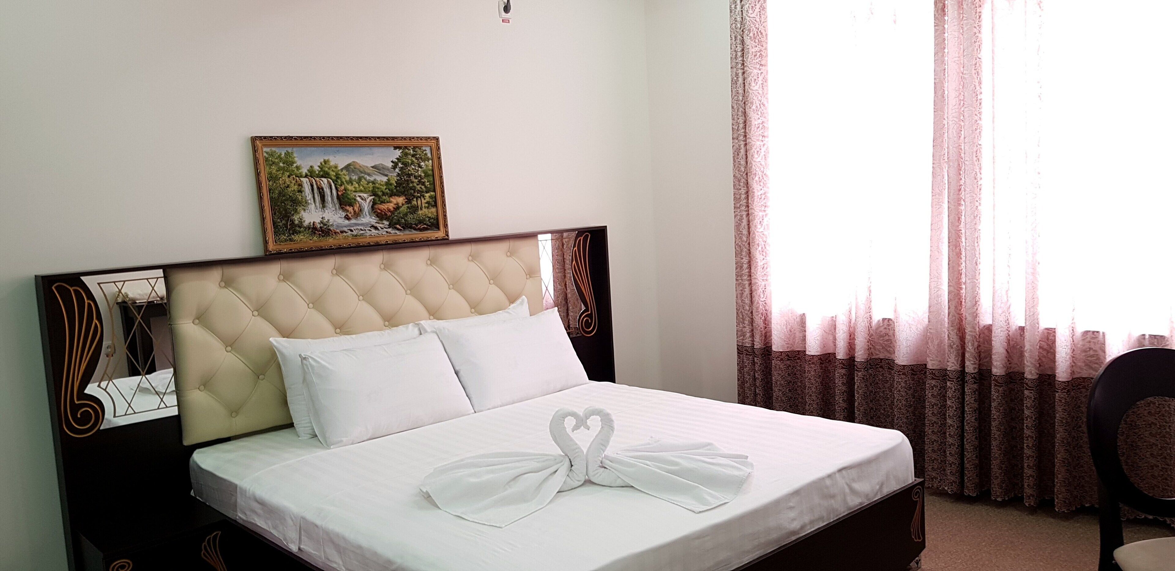 A neatly made bed with a white sheet and a decorative swan pillow. There is a framed picture of a waterfall on the wall above the bed.