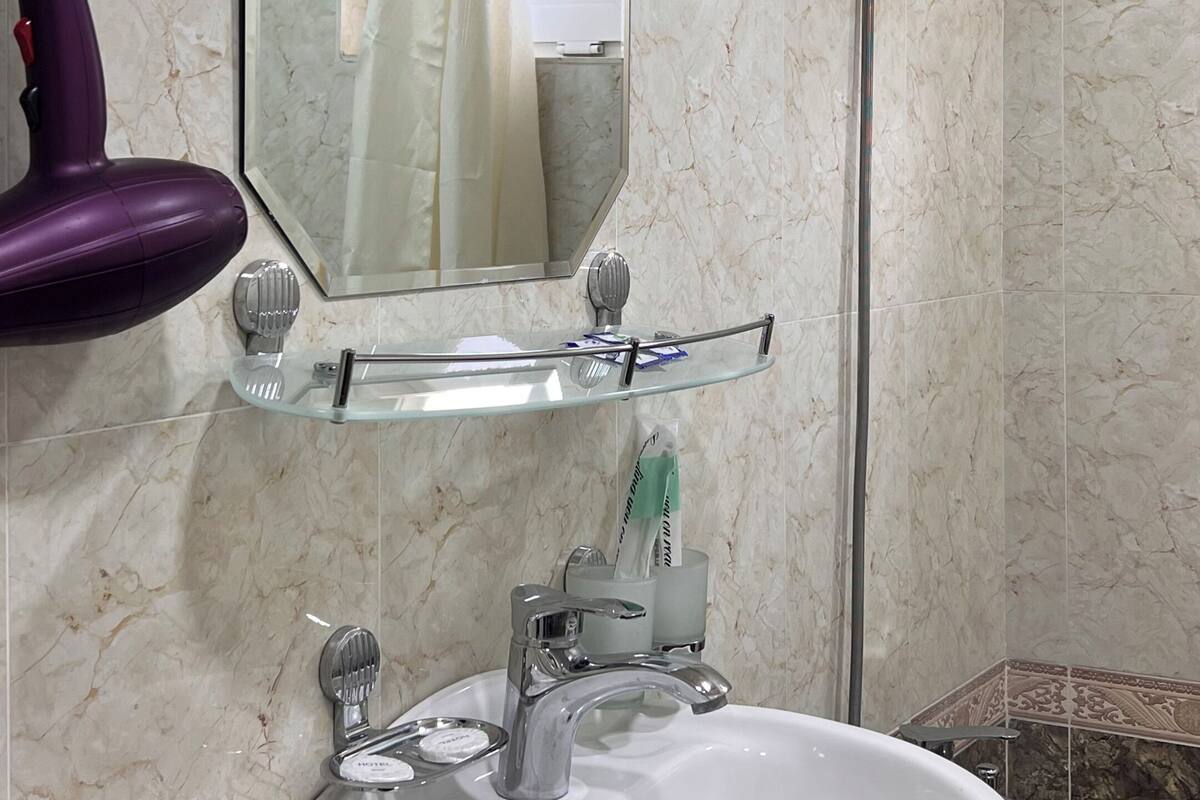 Ein Badezimmer mit Waschbecken, Spiegel, Dusche und einem violetten Föhn.