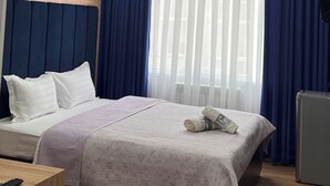 Et hotelværelse med seng, skrivebord, stol, fjernsyn og et vindue med gardiner.