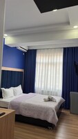 Habitación de hotel con cama, escritorio, silla, televisión y ventana con cortinas.