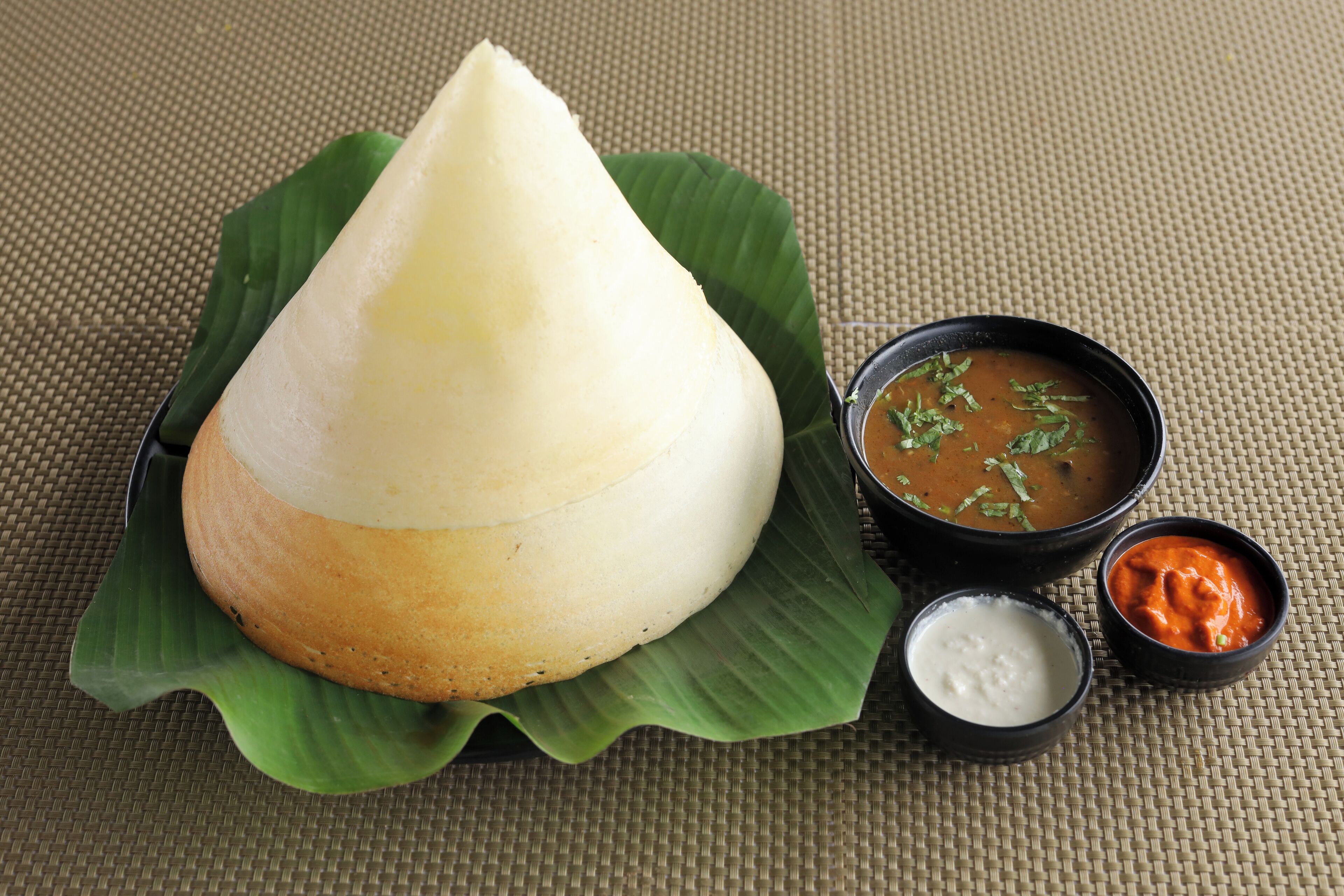 A traditional South Indian dish, Idli, served with three side dishes on a banana leaf.