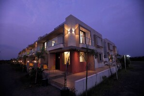 A modern multi-story residential building with balconies, large windows, and a well-lit entrance. - Leena Resort (Garudeshwar)