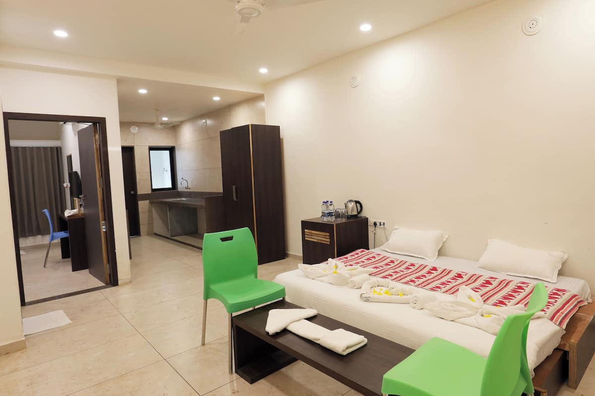A hotel room with a bed, green chairs, a desk, and a minibar.