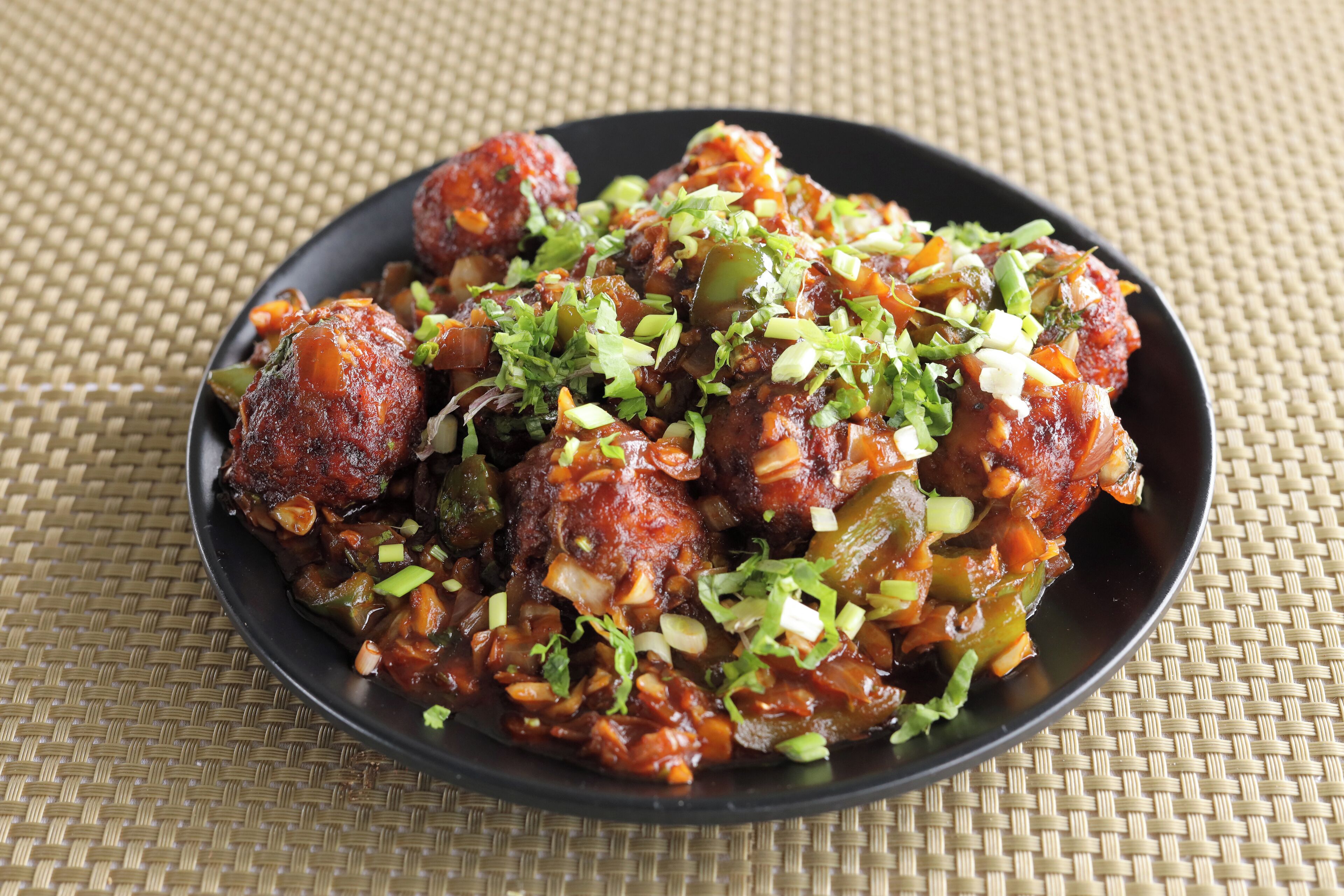 A plate of meatballs garnished with chopped green onions and herbs, served on a black plate.