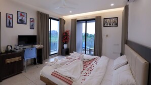 Habitación de hotel con cama, escritorio, silla, televisor y balcón con vistas.