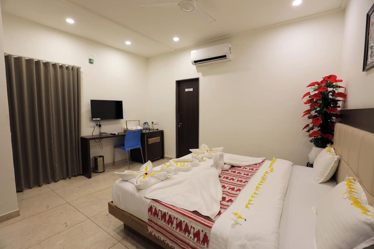 A hotel room with a bed, a desk, a chair, an air conditioner, a television, and a curtain.