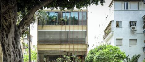 A multi-story building with balconies, a tree in the foreground, and parked motorcycles.