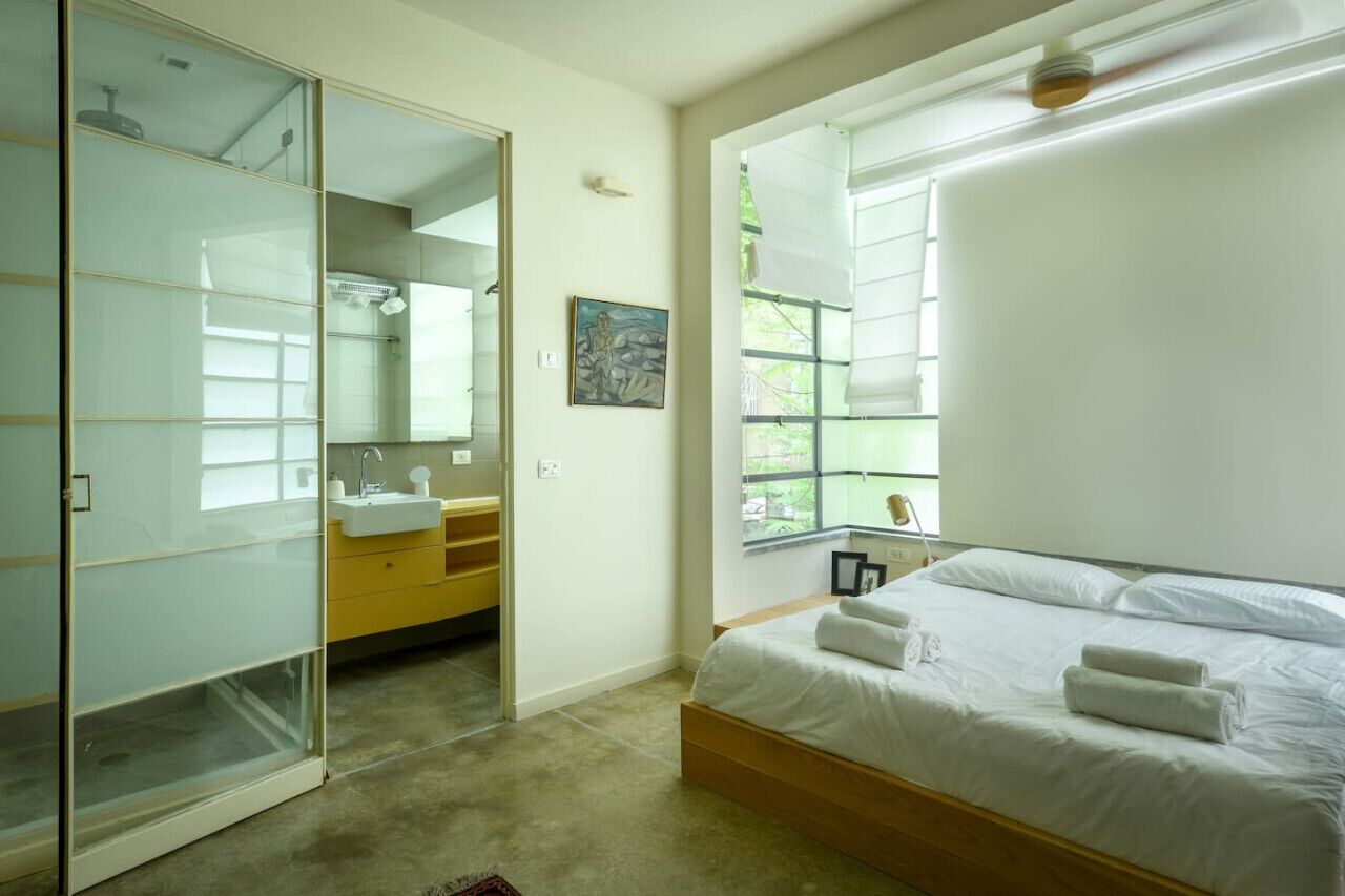 Quarto com cama, banheiro com pia e armário com porta de vidro deslizante.