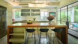 A modern kitchen with a central island, bar stools, and large windows offering a view of greenery. - Spacious & Green 3BR Apt w Balcony (Tel Aviv)