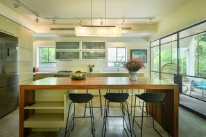A modern kitchen with a central island, bar stools, a refrigerator, and large windows.