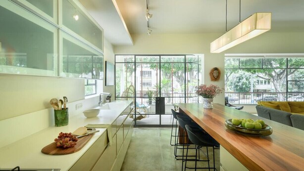 A modern kitchen with a large island, bar stools, and a view of the outdoors. - Spacious & Green 3BR Apt w Balcony (Tel Aviv)