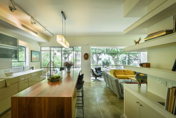 A modern kitchen with a wooden island, large windows, and a seating area with a yellow sofa.