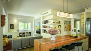 A modern kitchen with a wooden island, black bar stools, and a central island with a vase of flowers. - Spacious & Green 3BR Apt w Balcony (Tel Aviv)