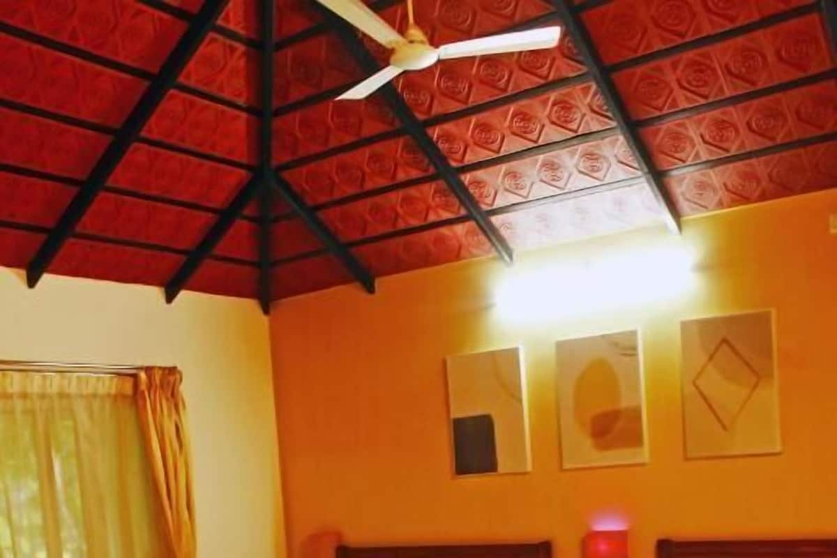 A hotel room with two beds, a wooden floor, a ceiling fan, and a window with curtains.