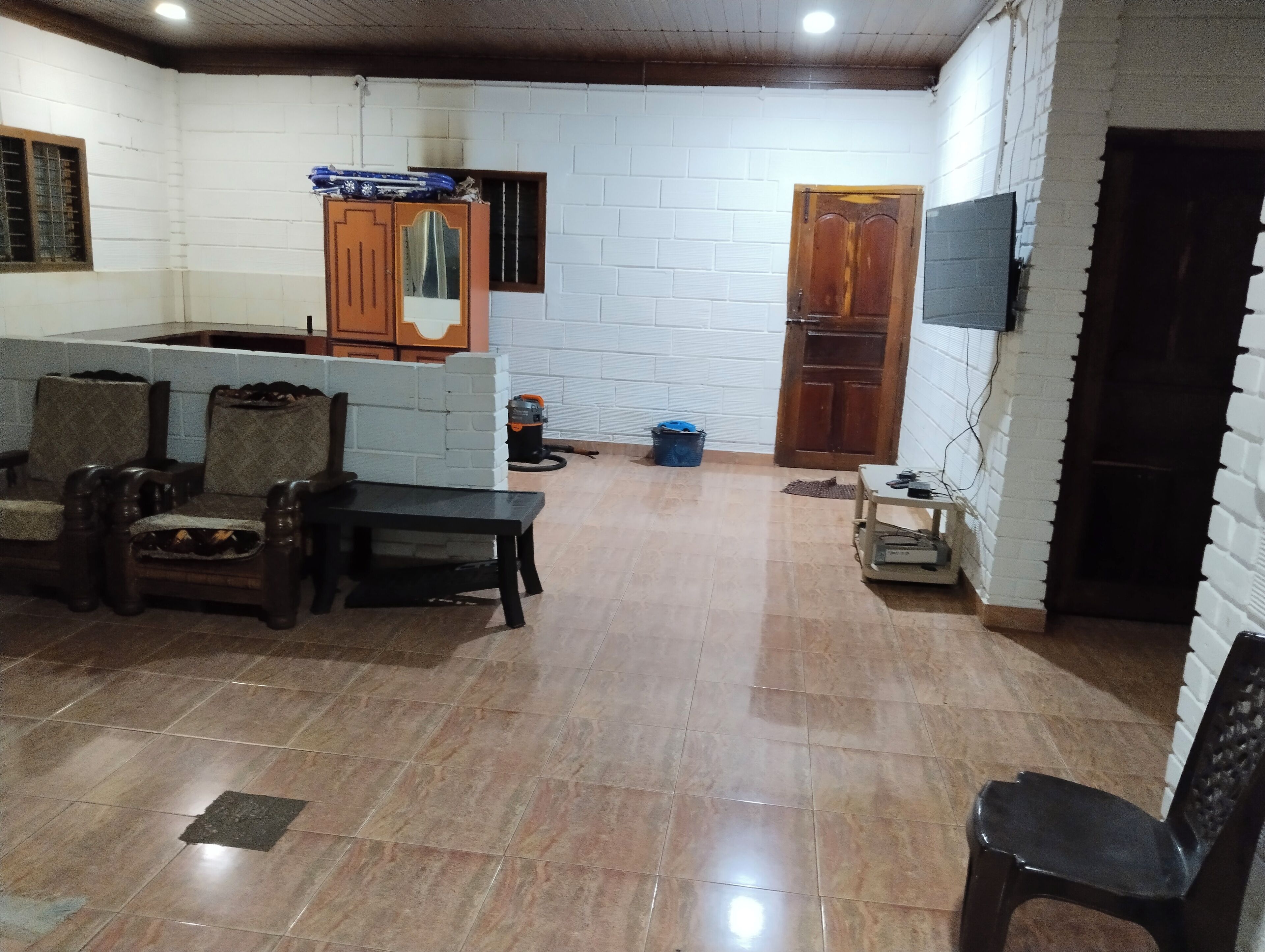 A room with a tiled floor, a wooden bench, a sofa, a small table, a television mounted on the wall, and a door.