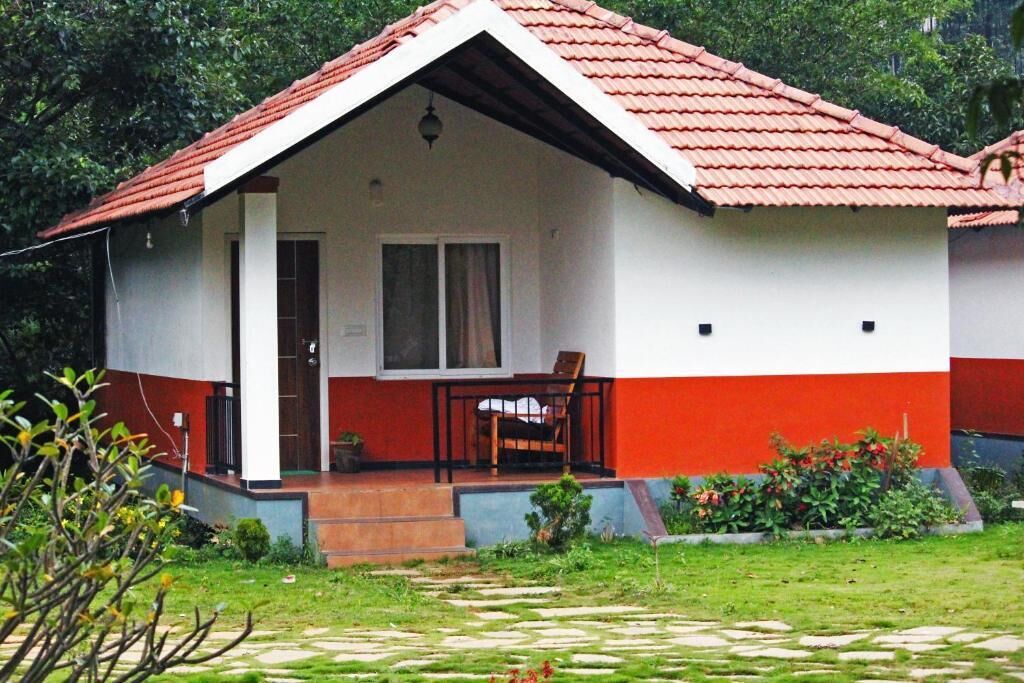 Une maison de plain-pied avec un toit recouvert de tuiles rouges, une véranda avec une chaise et un petit jardin.