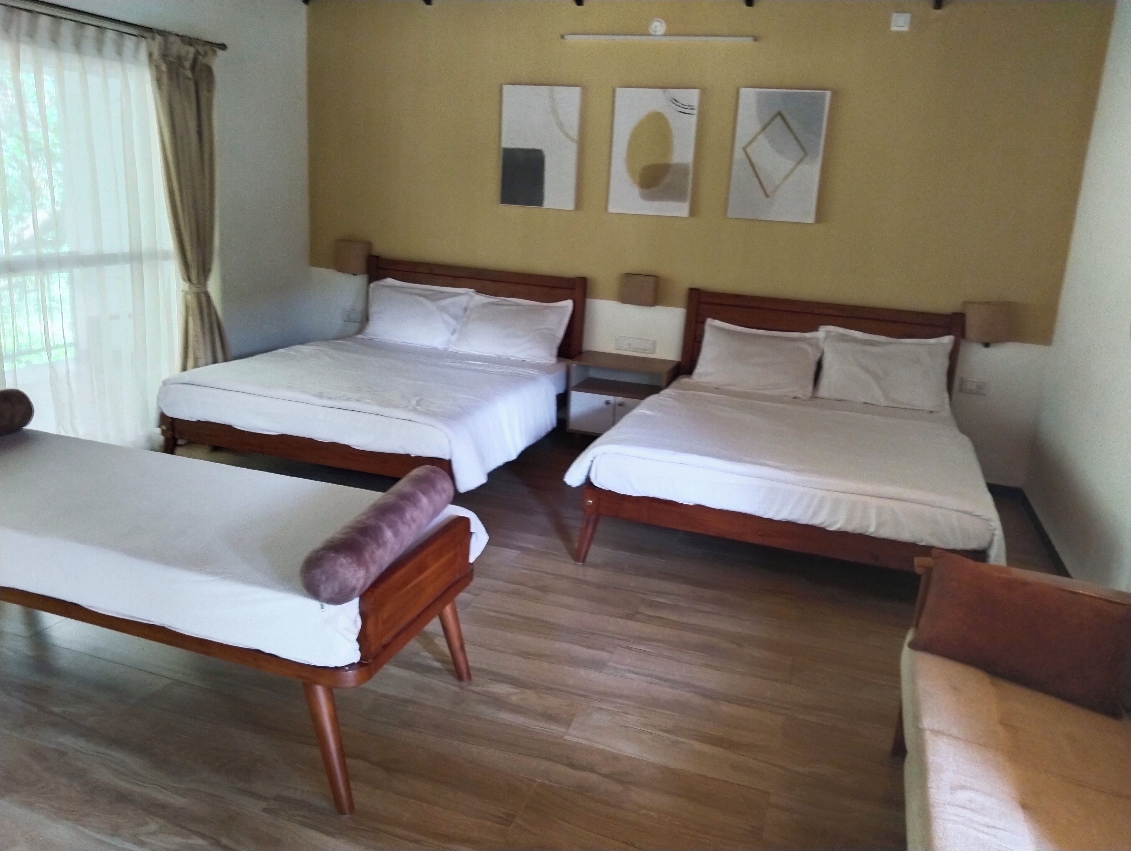 A hotel room with two single beds, a wooden floor, and a large window with curtains.