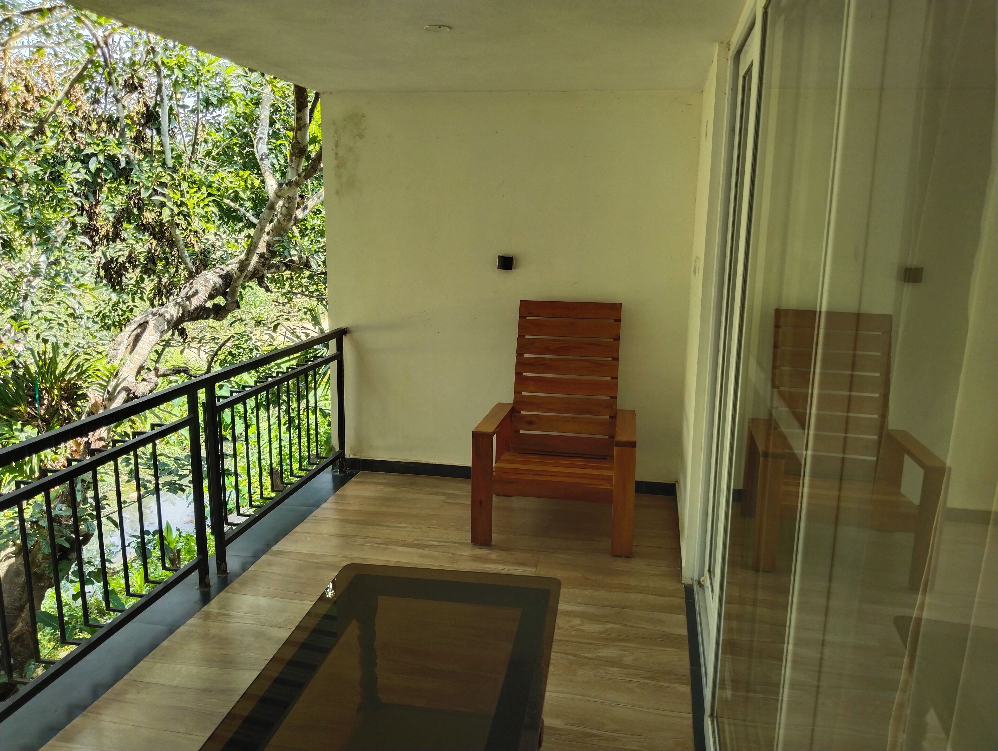 A balcony with a wooden chair, a glass door, and a view of greenery.