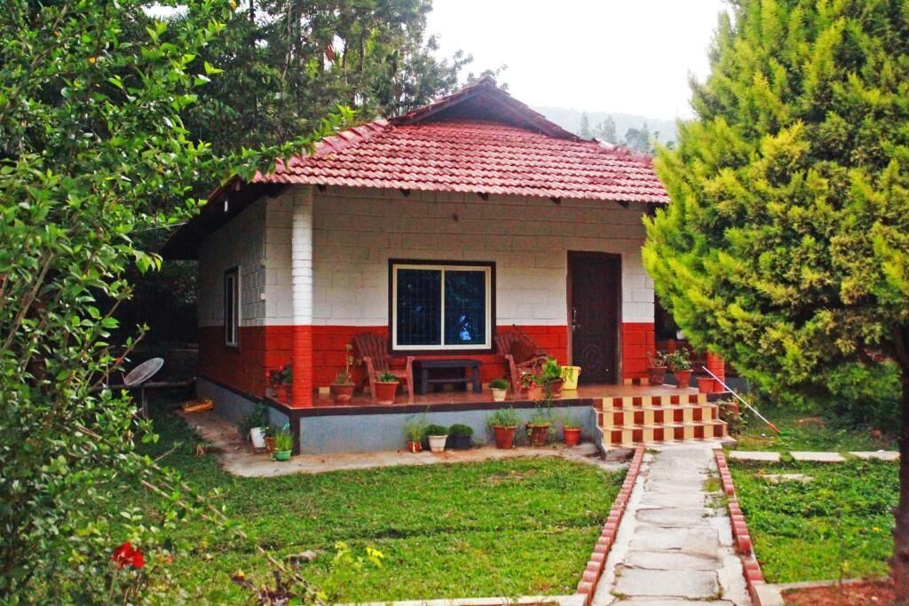 A house with a red-tiled roof, a front porch with potted plants, and a small garden area.