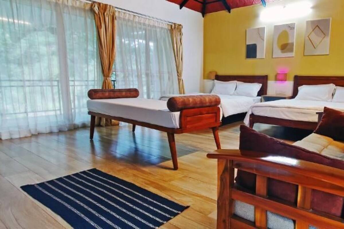 A room with two beds, a wooden sofa, and a large window with curtains.