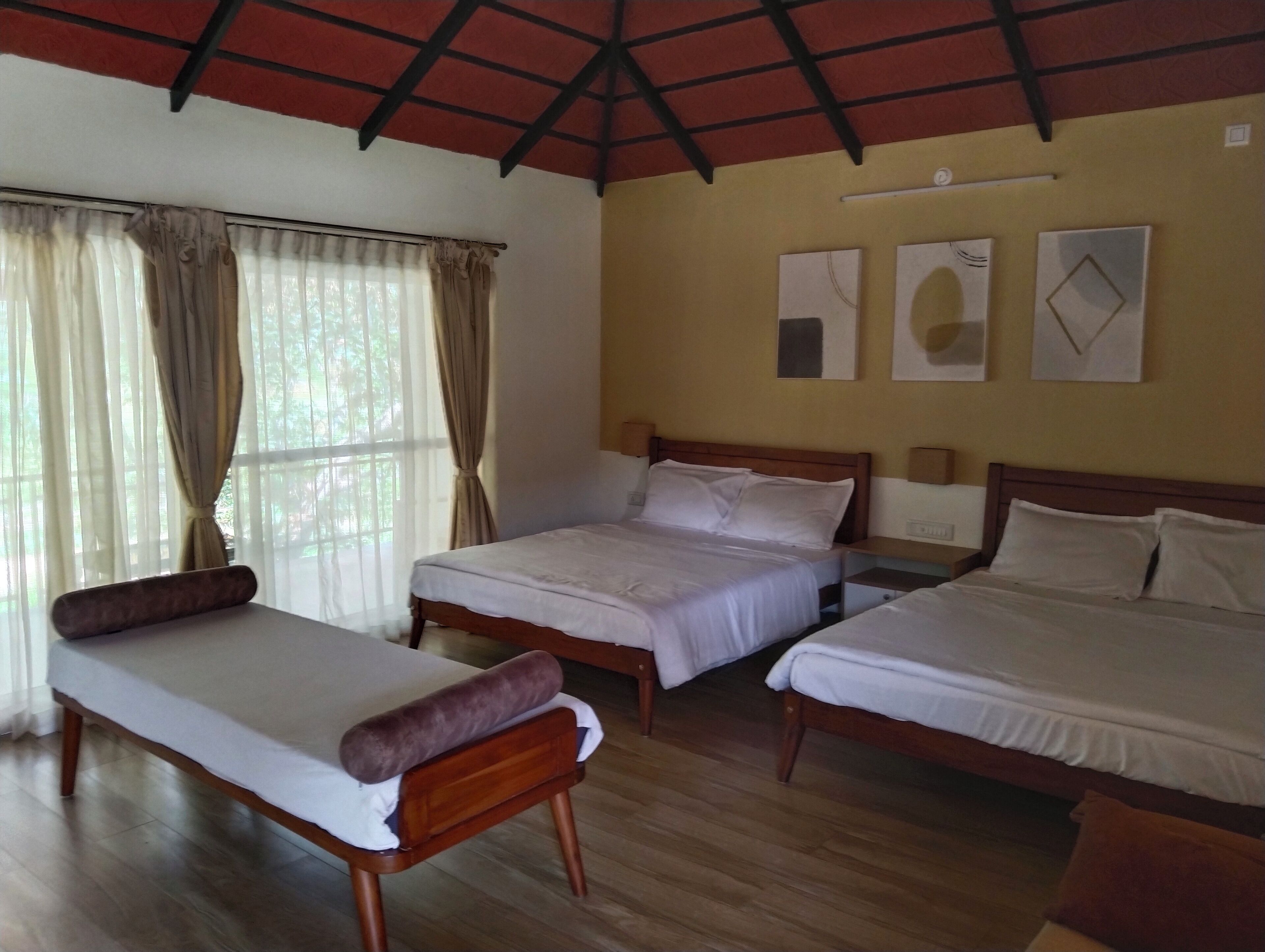 Une chambre d’hôtel avec trois lits simples, des têtes de lit en bois, un plancher en bois et une fenêtre avec des rideaux.