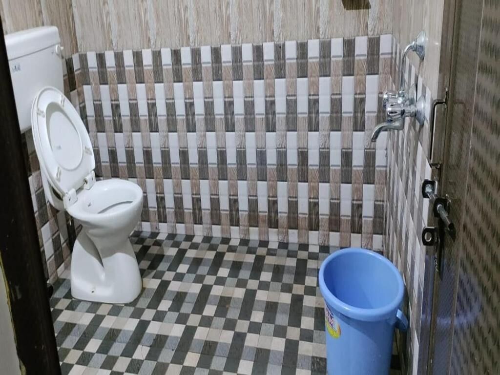 A bathroom with a checkered floor, a toilet, a shower area, and a blue bucket.