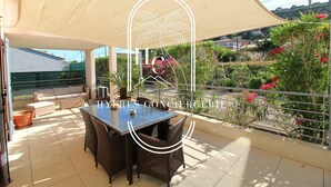 Un patio techado al aire libre con una mesa y sillas para comer, rodeado de abundante vegetación y flores.