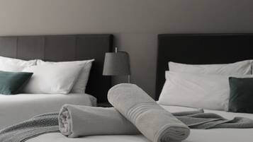 Una cama bien hecha con una toalla enrollada, dos almohadas blancas y una lámpara de color oscuro a su lado.
