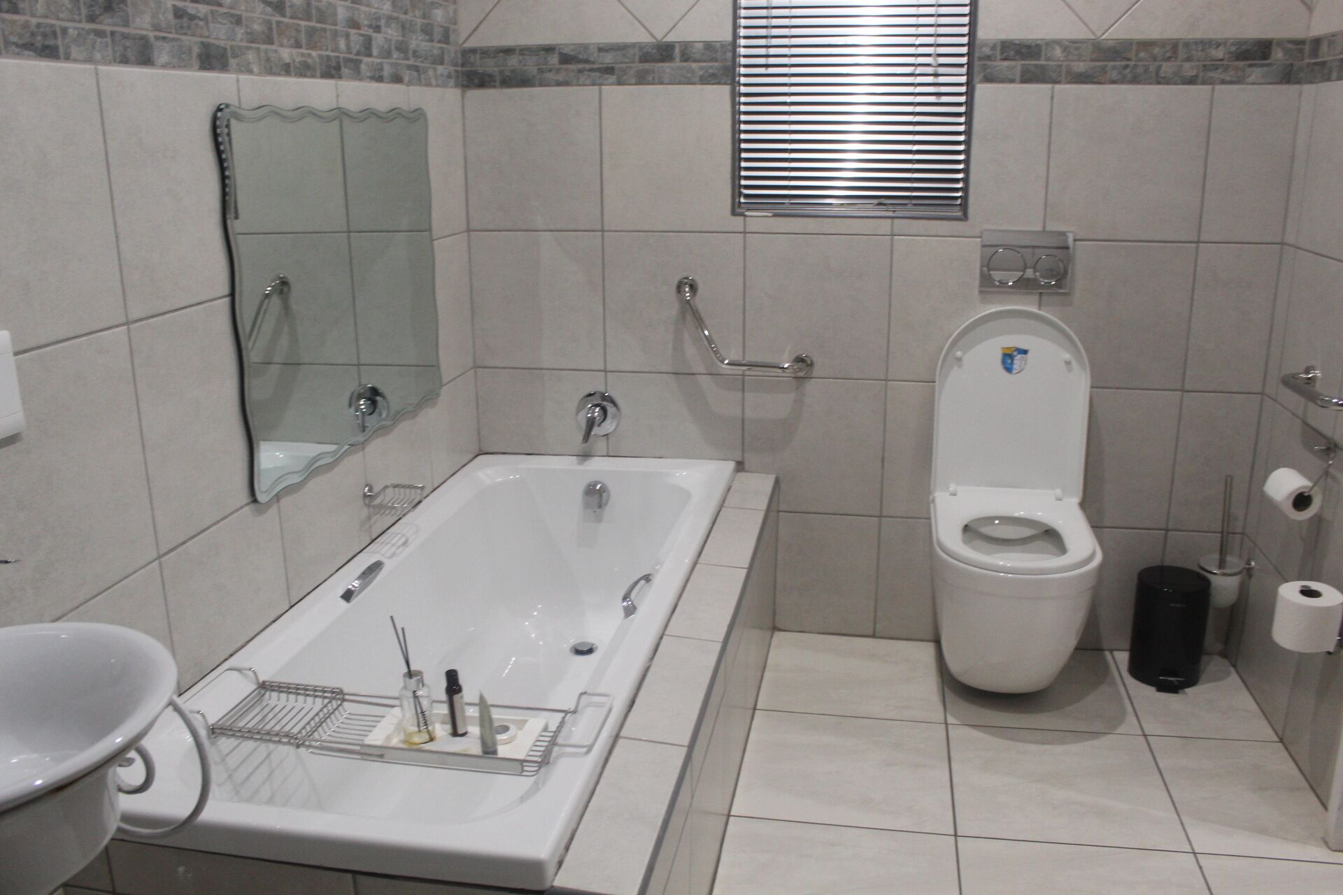 A bathroom with a bathtub, toilet, and a handrail.