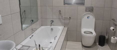 A bathroom with a bathtub, toilet, and a handrail.