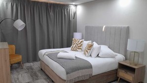 Ett modernt hotellrum med en stor säng, ett sängbord, en lampa och en stol.
