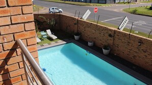En hotellpool med en mur av tegelsten, solstolar och en stoppskylt.