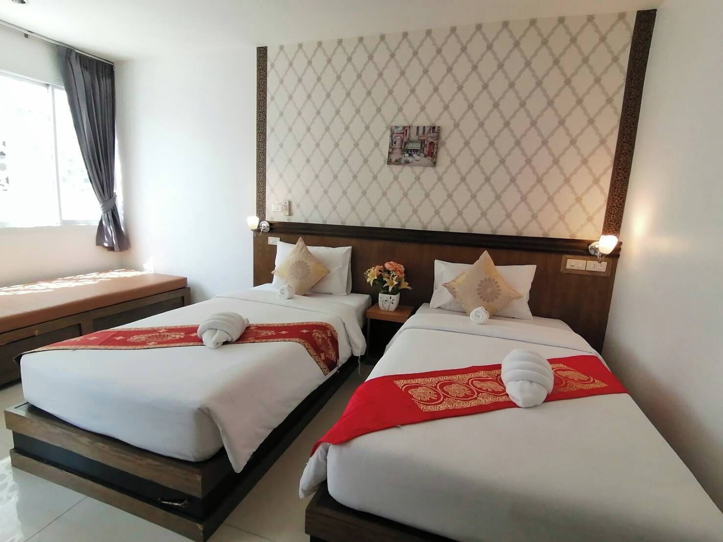 Habitación de hotel con dos camas, cada una con una colcha roja y blanca, almohadas blancas y una mesita de noche con un jarrón de flores.