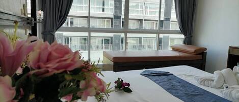 A hotel room with a large bed, a window with curtains, a bedside table, and a view of a building outside.