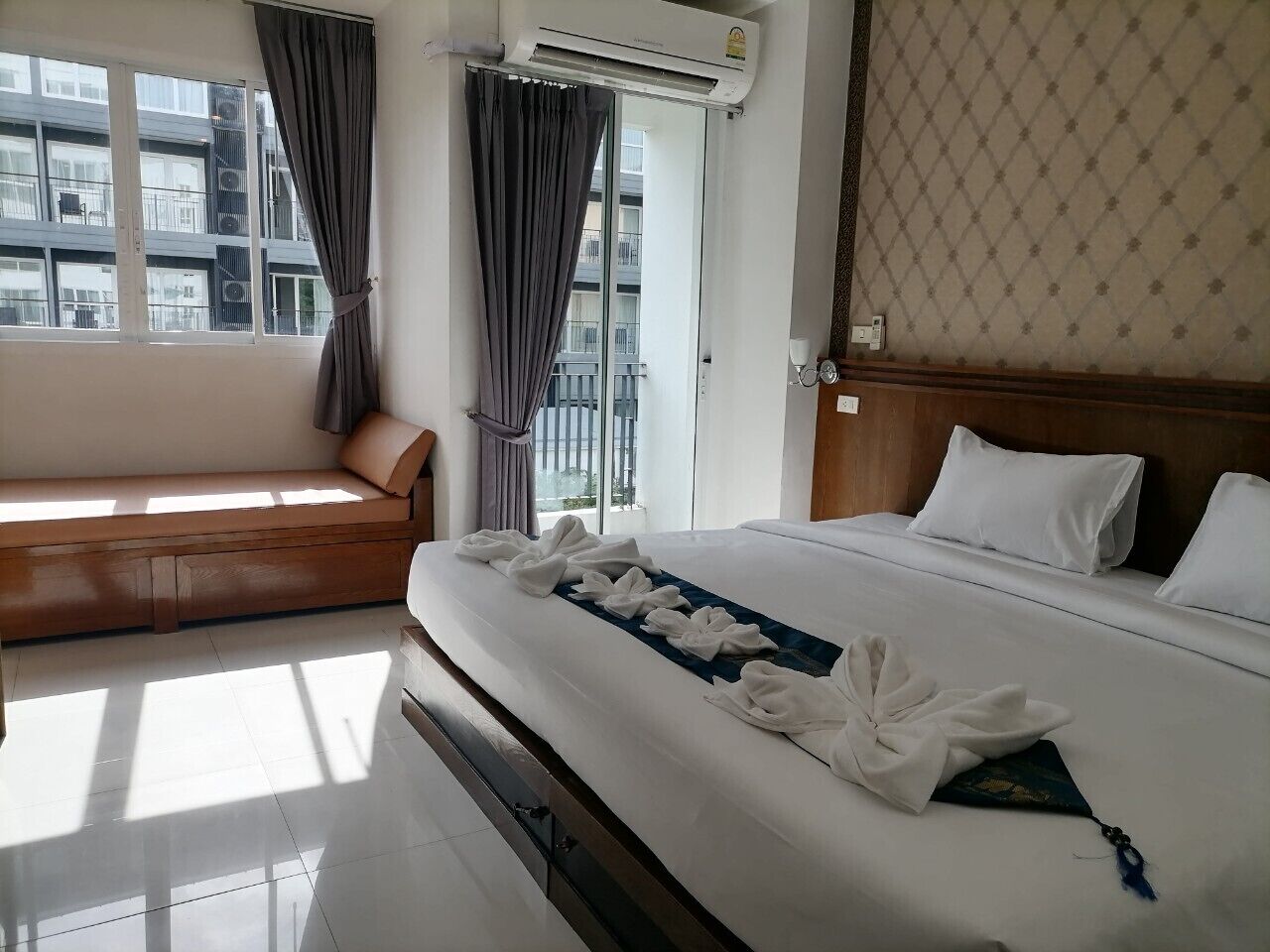 A hotel room with a bed, a sofa, an air conditioning unit, and a window with curtains.