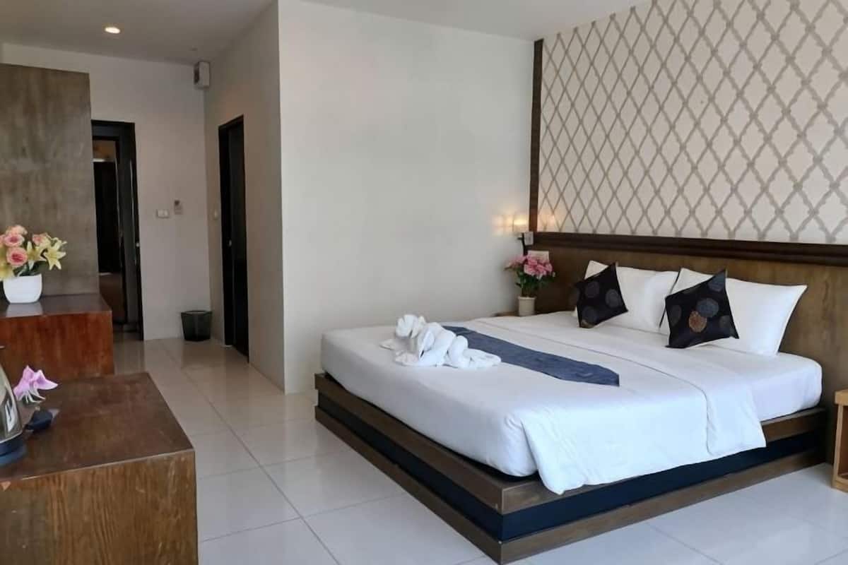 A hotel room with a large bed, a wooden headboard, a desk with a vase of flowers, and a patterned wall.