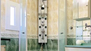 Kulmassa sijaitseva kylpyhuone, jossa on lasiseinällä varustettu suihku, peilillä varustettu pesuallas ja wc.