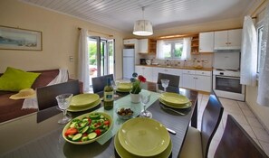 A modern kitchen with white cabinets, a dining table set for four, and a view of the outdoors through the window. - Nyktelia Holiday Villa (Lefkada)