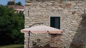 Ein Gebäude aus Stein mit einem Ziegeldach, einem Tisch mit Sonnensegel und einem Blumentopf.