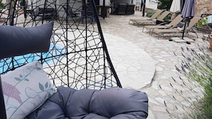 A cozy outdoor seating area with a swing chair, lounge chairs, and a stone-paved patio. - Lavender Hill Hvar (Stari Grad)