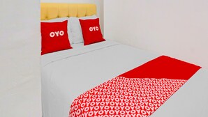 A bed with a yellow headboard, two red pillows with "OYO" text, and a red blanket with a white pattern. - Hotel O Btc Guest House Syariah (Malang)