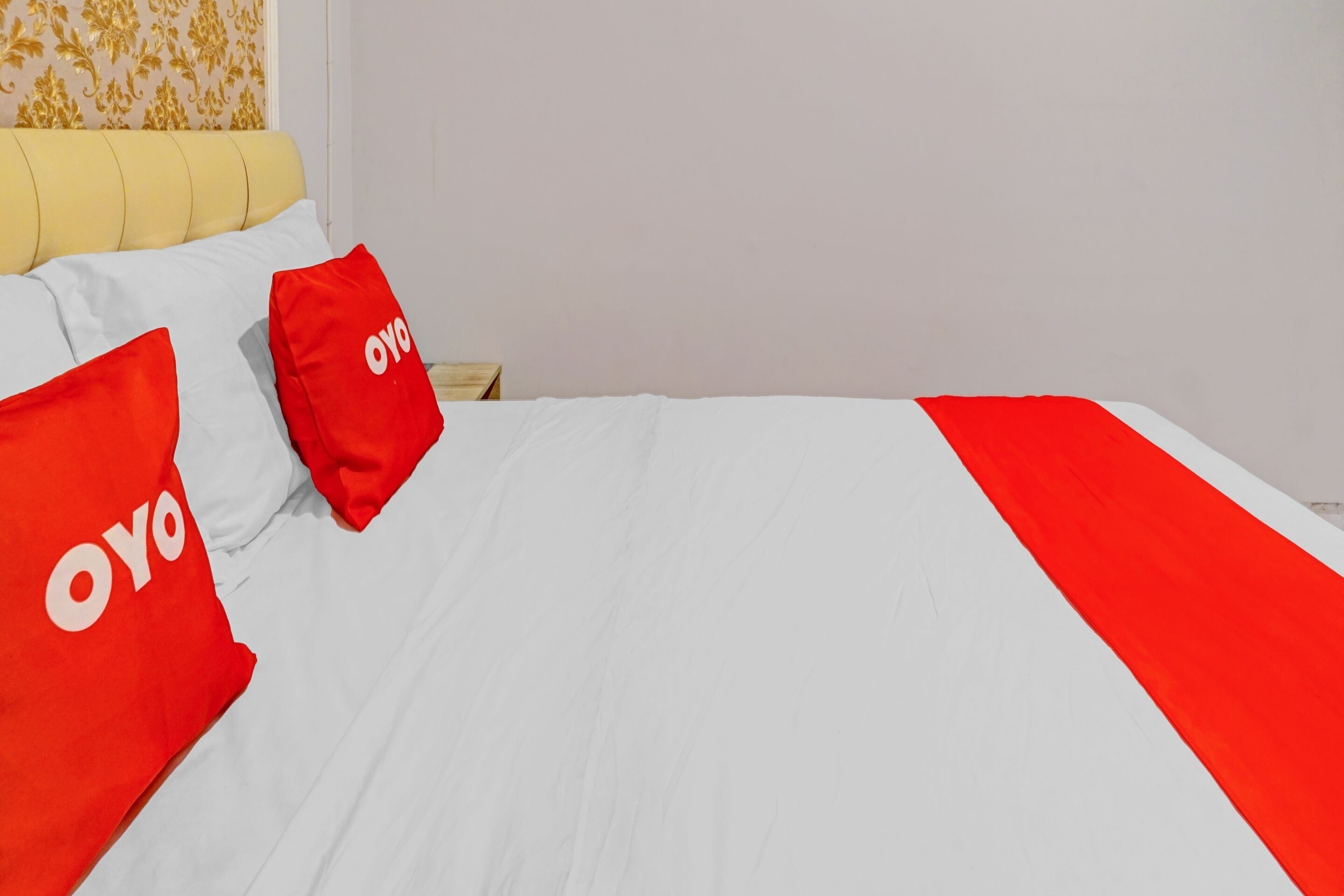 Un lit avec une literie blanche et rouge, deux oreillers rouges ornés du mot « oyo », et une tête de lit jaune.