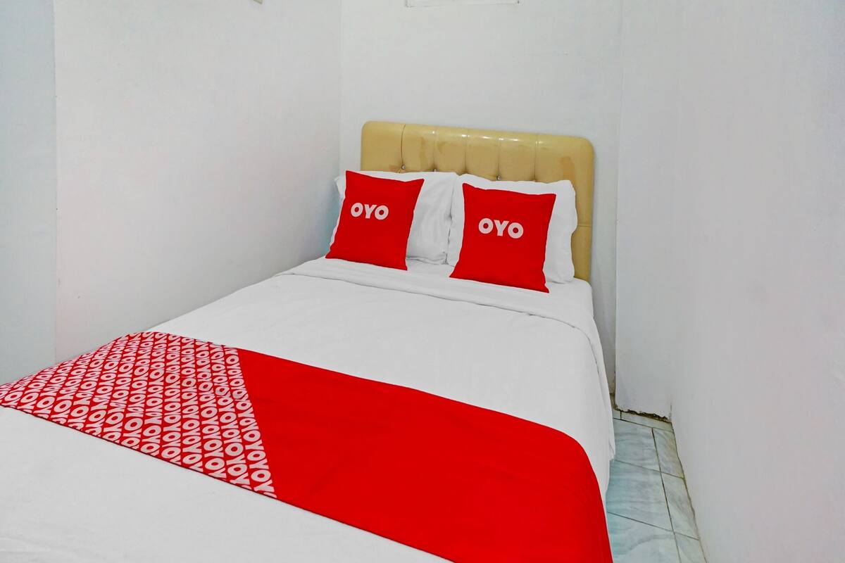 Un lit recouvert d’une couvre-lit blanche et rouge, deux oreillers rouges ornés du mot « OYO », et une tête de lit de couleur beige.